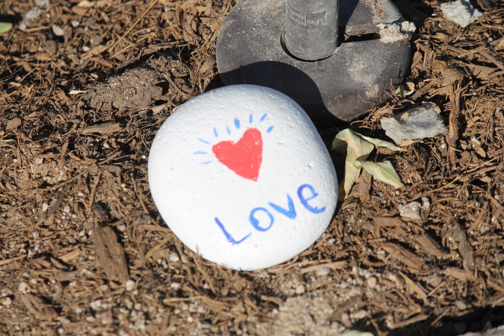 white rock laying on brown ground, with the word Love written on it in blue, and a small red heart
