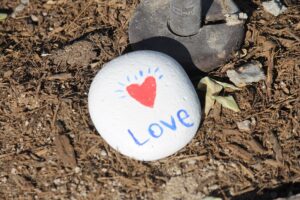 white rock laying on brown ground, with the word Love written on it in blue, and a small red heart